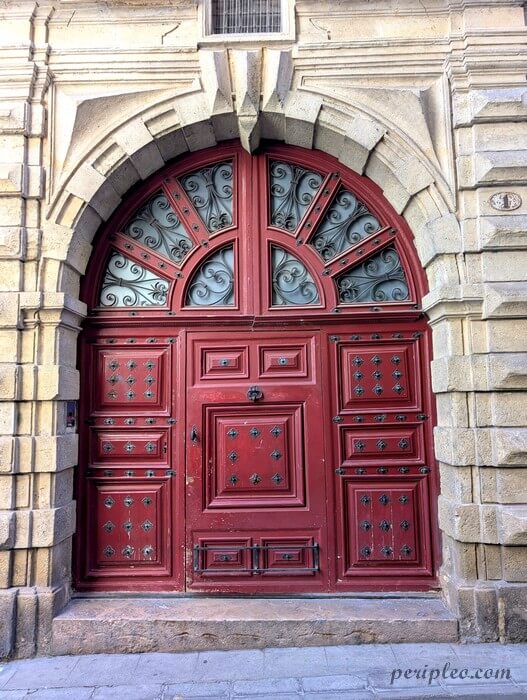 Grande porte rouge sculptée de l’Hôtel de Solas à Montpellier encadrée de pierre et ornée de ferronneries anciennes