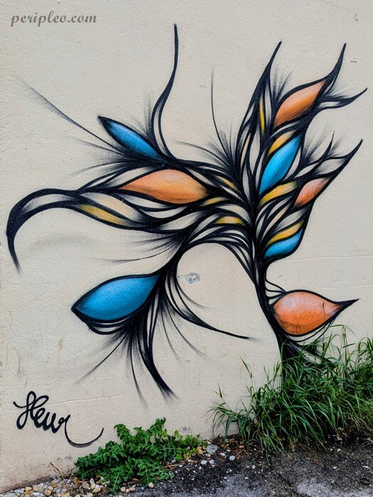 Street art signé Fleur Avenue du Pont Juvénal à Montpellier, fresque végétale abstraite aux teintes bleues et orangées réalisée sur un mur du Quartier Antigone