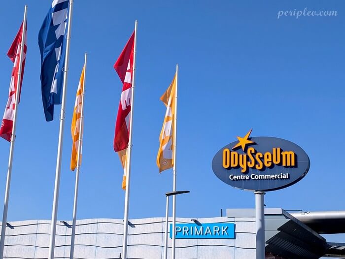 Entrée d’Odysseum à Montpellier, centre commercial et de loisirs avec enseignes et drapeaux sous le ciel bleu