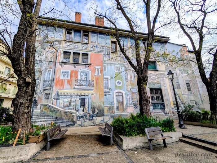 Street art Place François Jaumes à Montpellier avec vaste fresque en trompe-l’œil représentant les façades historiques du Quartier Méditerranée sur un immeuble résidentiel