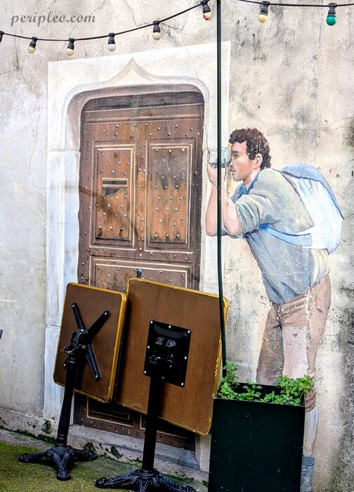Street art Place Saint-Roch à Montpellier avec fresque en trompe-l’œil signé Mad'Art représentant un personnage prenant une photo dans le centre historique sud