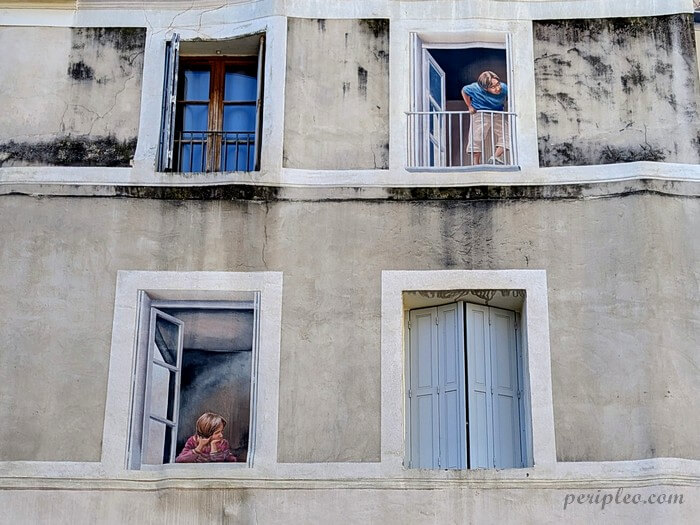 Fresque en trompe-l’œil signé Mad'Art Place Saint-Roch à Montpellier, personnages aux fenêtres d’une façade du centre historique sud