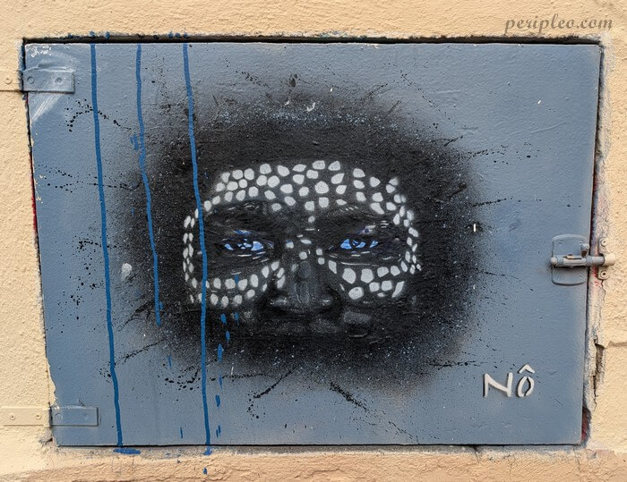 Street art Rue Isidore Girard à Montpellier, portrait au pochoir aux yeux bleus et motifs blancs réalisé par Nô sur une porte métallique du Quartier Méditerranée