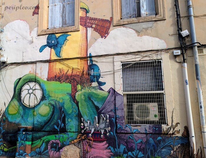 Œuvre monumentale de Street art dans la Rue Méditerranée à Montpellier, imaginée par Nubian, représentant un paysage onirique avec oiseaux, végétation et personnages fantastiques sur une façade ancienne du Quartier Méditerranée