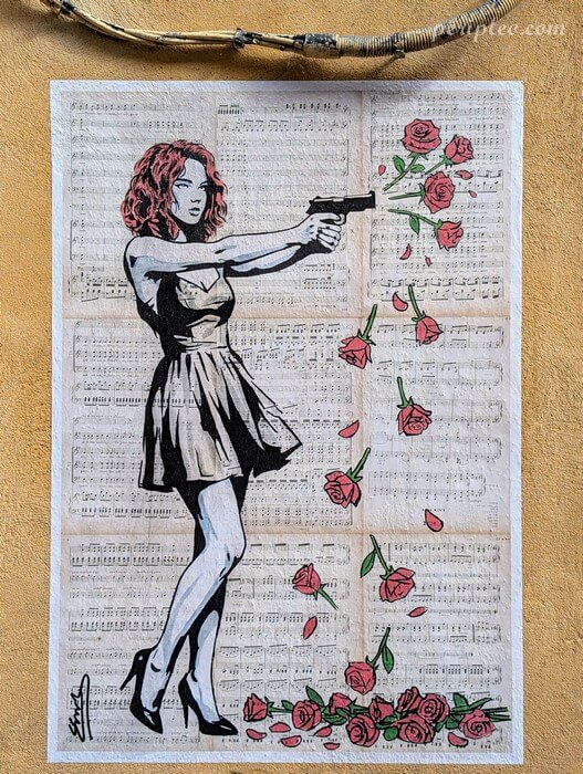 Collage de street art dans la Rue Méditerranée à Montpellier montrant une femme armée dont les tirs se changent en roses, sur fond de partitions musicales
