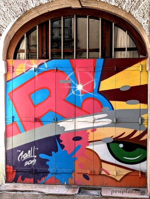 Porte colorée décorée d’un graffiti aux couleurs vives Rue du Plan de l’Olivier à Montpellier, mêlant lettrage urbain et regard expressif dans un style street art contemporain dans le centre historique nord