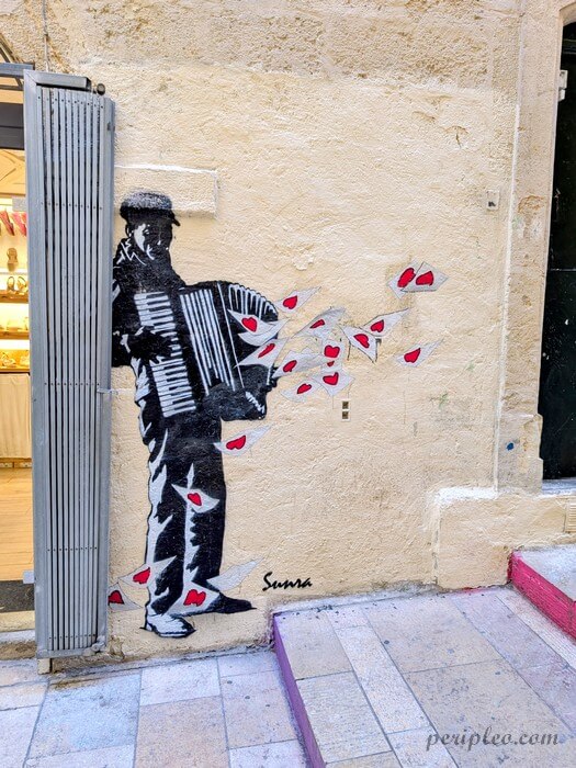 Street art Rue du Bras de Fer à Montpellier avec une œuvre de Sunra avec musicien à l’accordéon et envolée de cœurs rouges dans le centre historique sud