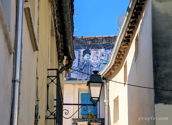 Œuvre de street art visible au-dessus des toits de la Rue Claude Serres à Montpellier, représentant un personnage inspiré de l’univers du dessin animé dans une ruelle du centre historique nord