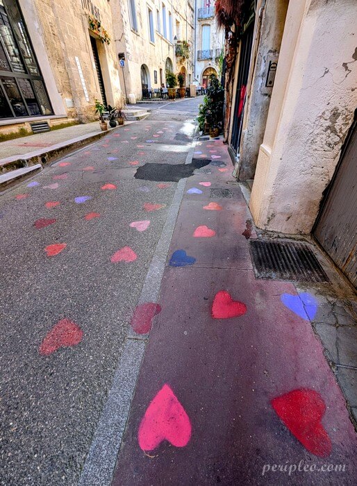 Street art Rue Glaize à Montpellier, pluie de cœurs rouges, roses et violets peints au sol, une intervention urbaine poétique qui guide les passants à travers les ruelles du centre historique nord