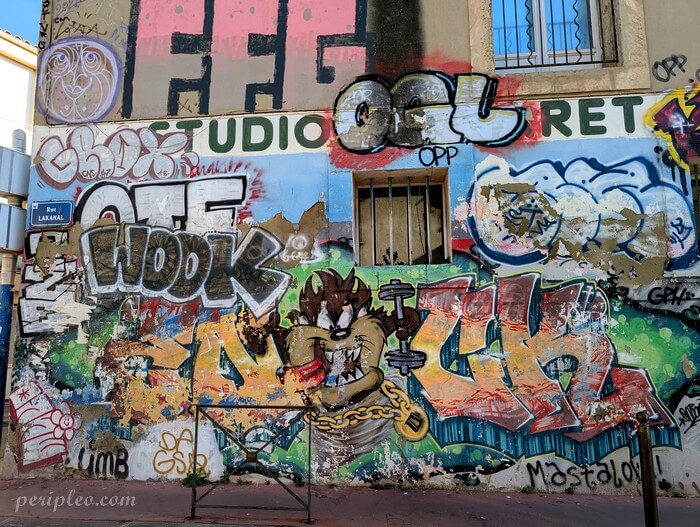 Street art Rue Lakanal dans le Quartier des Beaux-Arts à Montpellier, mur entièrement recouvert de graffitis colorés où un personnage inspiré de Taz, le diable de Tasmanie, s'impose au milieu des lettrages et fresques emblématiques de la scène urbaine locale