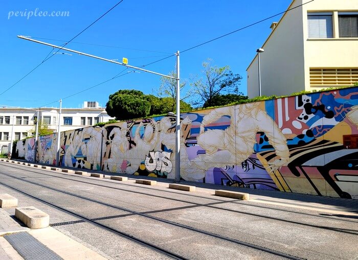 Street art Rue du Pont de Lattes à Montpellier, longue fresque murale colorée bordant les voies du tramway mêlant personnages, formes abstraites et graffitis contemporains avec le soutien de la galerie Nicolas Xavier