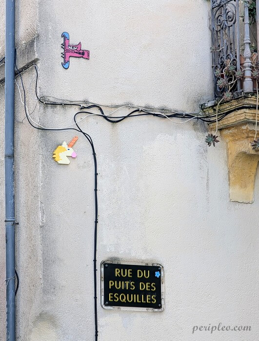 Street art Rue du Puits des Esquilles à Montpellier, clin d'œil ludique à l'univers du pixel art avec de petites mosaïques colorées disséminées autour de la plaque de rue dans le centre historique nord