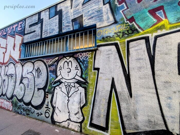 Street art coloré dans la Rue de la Substantion à Montpellier, représentant un personnage dessiné au milieu de grandes fresques de graffiti dans le Quartier des Beaux-Arts
