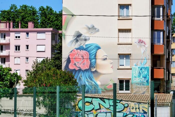 Street art à la Cité des Jardins à Montpellier, immense fresque murale signée Sweo et Nikita représentant une femme au regard tourné vers l'horizon, coiffée d'une rose et entourée de poissons flottants