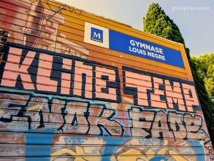 Street art au Gymnase Louis Nègre à Montpellier, immense rideau métallique recouvert de lettrages graffiti monumentaux aux contours noirs et aux teintes rose, argent et bleu