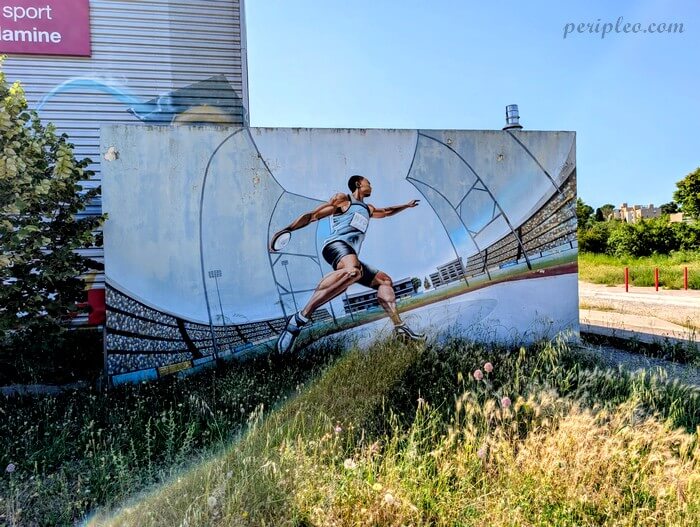 Fresque de street art représentant un athlète en pleine course sur un mur de la Halle des Sports La Condamine à Montpellier