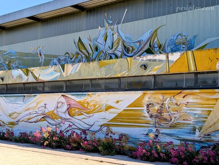 Murale de street art sur la Halle des Sports La Condamine à Montpellier, représentant un athlète en pleine course et saut dynamique sur fond graphique jaune et bleu
