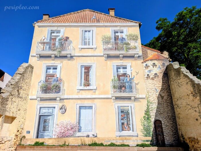 Fresque en trompe-l’œil par l'atelier A-Fresco au Parc Clémenceau à Montpellier, façade peinte avec habitants aux balcons dans un décor urbain