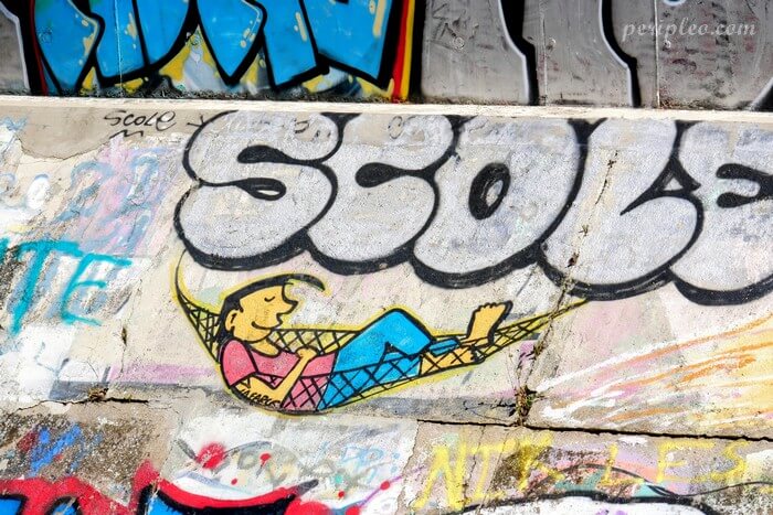 Petit personnage allongé dans un hamac sous un graffiti au Quai du Verdanson, haut lieu du Street art à Montpellier