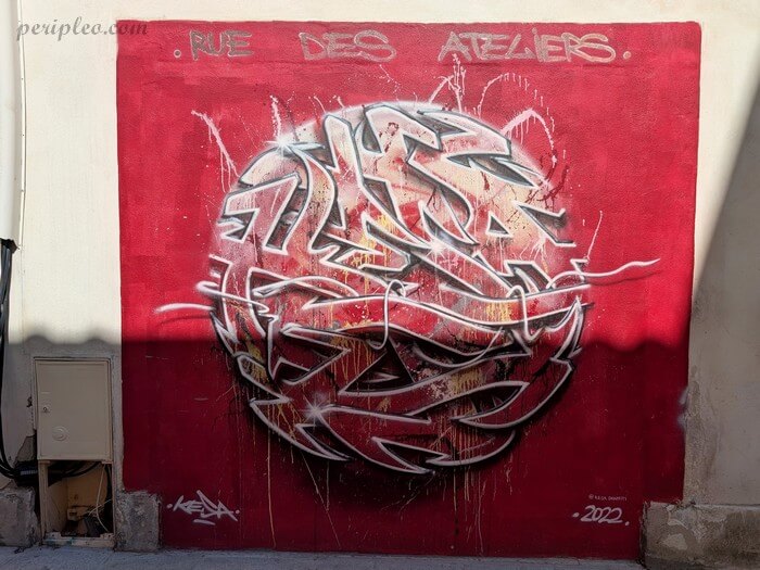 Street art Rue des Ateliers à Montpellier avec graffiti abstrait rouge et blanc sur fond écarlate de Kesa dans le quartier créatif de la ville