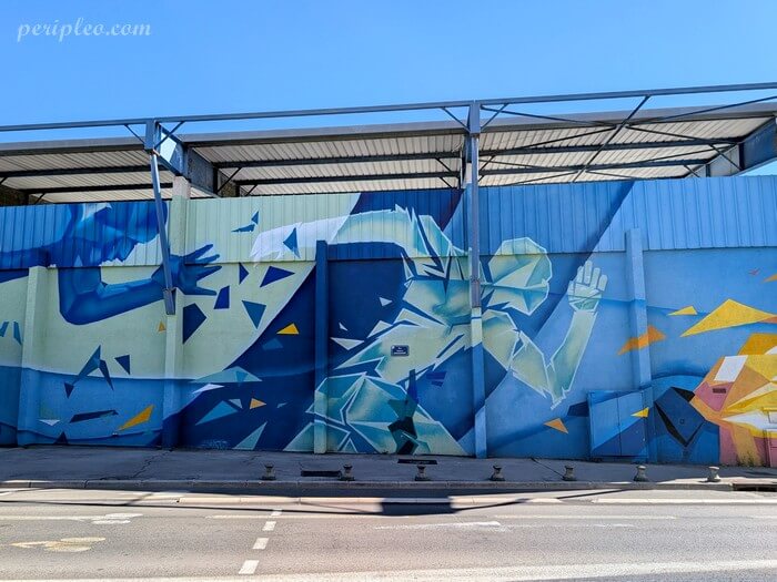 Street art au Stade Philippidès à Montpellier, immense fresque aux dominantes de bleu du collectif Bombing Colors représentant des silhouettes de sportifs décomposées en formes géométriques