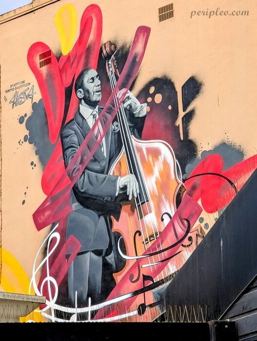 Fresque de street art de Hista représentant un musicien jouant de la contrebasse, sur un mur de l’Avenue d’Assas à Montpellier, avec des touches graphiques rouges et jaunes dynamiques