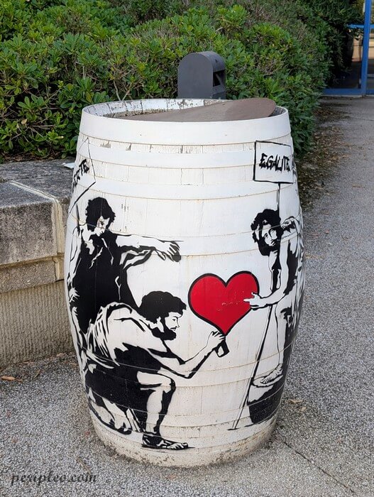 Street art au Château d'Alco à Montpellier, œuvre de Sunra peinte sur un tonneau urbain représentant plusieurs personnages s'unissant pour peindre un grand cœur rouge