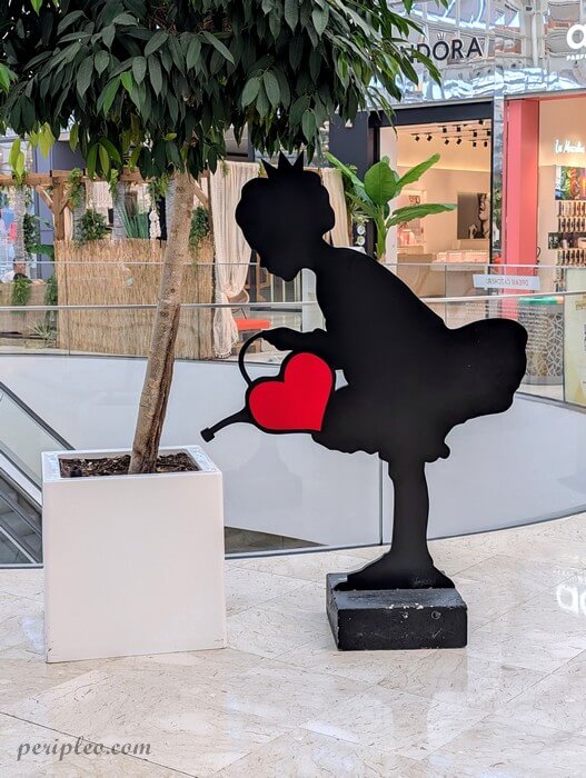 Street art au Polygone de Montpellier, œuvre de Sunra représentant une petite princesse tenant un arrosoir en forme de cœur rouge dans le centre commercial