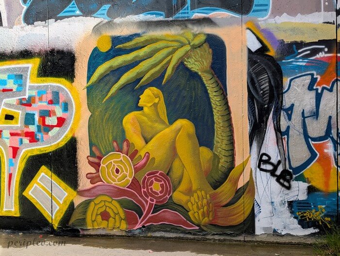 Street art Quai du Verdanson à Montpellier, fresque représentant une silhouette dorée se reposant sous un palmier, entourée de végétation tropicale