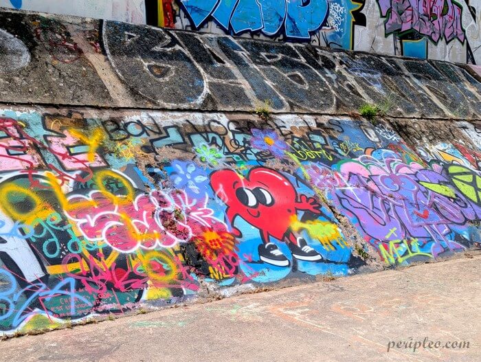 Street art Quai du Verdanson à Montpellier, composition haute en couleur mêlant graffitis, lettrages et un cœur rouge anthropomorphe au sourire malicieux