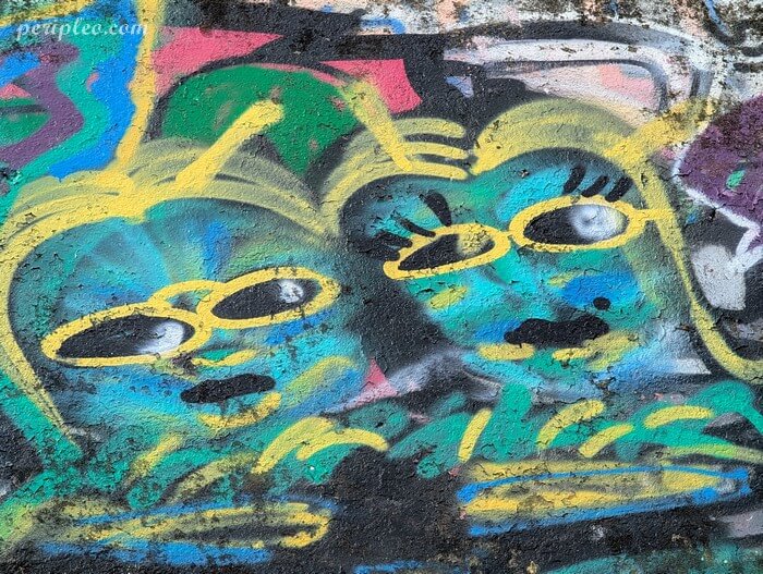 Street art Quai du Verdanson à Montpellier, portrait de deux visages stylisés aux teintes bleu-vert, soulignés de traits jaunes et de regards énigmatiques