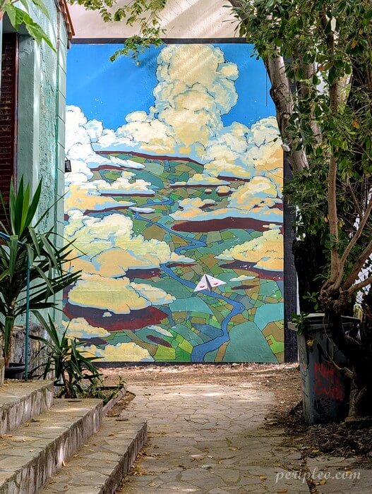 Street art Rue Marcel de Serres à Montpellier, fresque monumentale de l'Atelier Parcours représentant un paysage vu du ciel, traversé par une rivière serpentant entre les champs sous un immense ciel parsemé de nuages